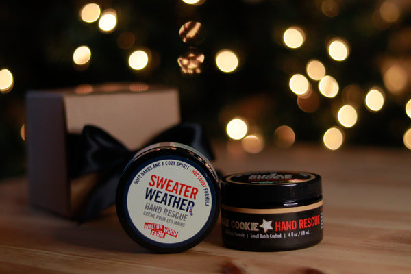 Sweater Weather hand balm on a wood table with glowing holiday lights