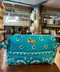 A turquoise blue and white paisley bandana pouch bag sits on a wooden counter inside a retail store.