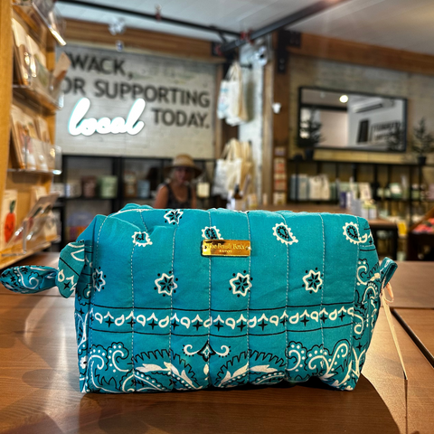 A turquoise blue and white paisley bandana pouch bag sits on a wooden counter inside a retail store.