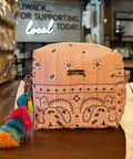 A pink bandana-patterned cosmetic pouch with a tassel charm sits on a wooden counter inside a retail store.
