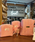 Three pink polka-dot fabric pouches with bow details are displayed on a wooden counter inside a boutique setting.
